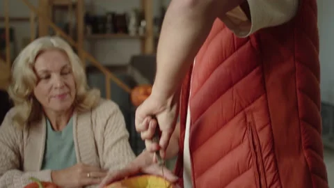 A man cuts a pumpkin with a knife at the table. A wishing woman sits at the Stock Footage 163253780