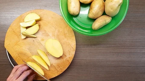 A man cuts raw potatoes on a round Board with a kitchen knife. The view from Stock Footage 128839072