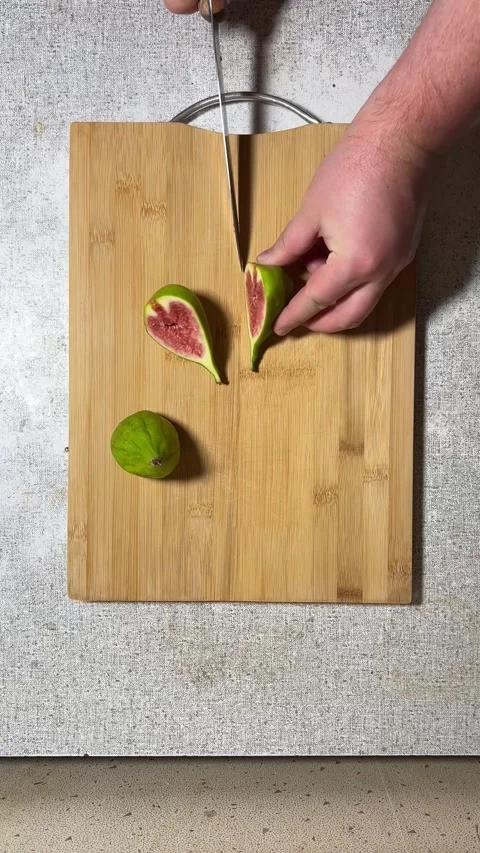 Man cuts raw sweet fresh juicy green fig on gray plate on wooden cutting board Stock Footage 280854008