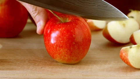 Man cuts red apple with kitchen knife on wooden board Stock Footage 128333467