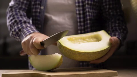 Man cuts ripe melon into slices on wooden cutting board using knife. Juicy fruit Stock Footage 319340024