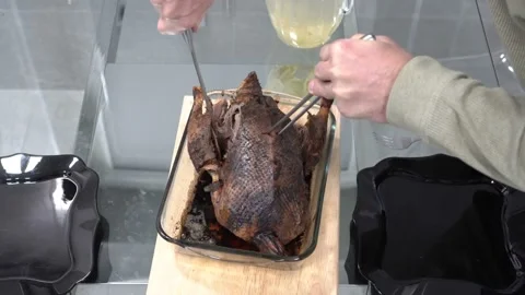 A man cuts a roast duck with a large kitchen knife on a wooden cutting board Video stock 125389719