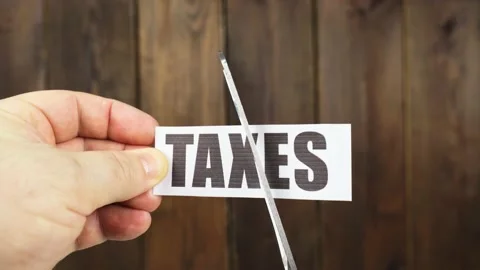 A man cuts with scissors a strip of paper with the inscription - TAXES Stock Footage 229417202