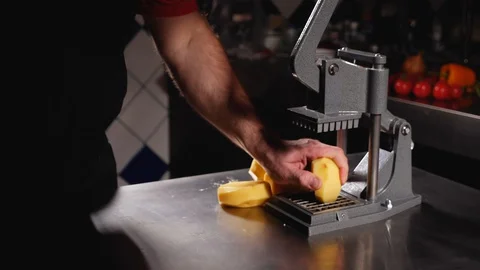 A man cuts several peeled potatoes with a big french fries cutter.Close up. Stock Footage 128294885