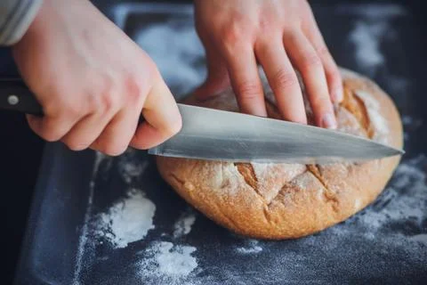 A man cuts with a sharp knife freshly made homemade wheat bread lying on a da Stock Photos