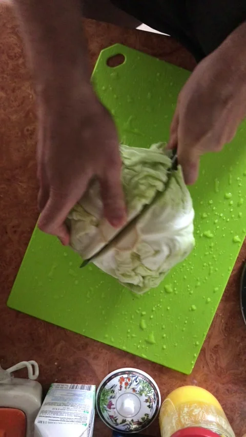 A man cuts a small cabbage on a plank into two halves with a large knife Stock Footage 241180168