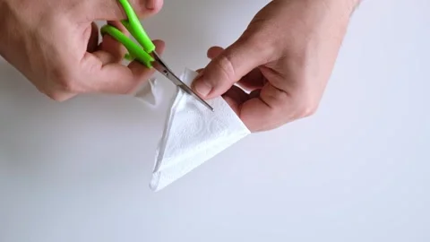 Man cuts a snowflake out of a paper napkin with scissors. Making paper crafts Stock Footage 323176179