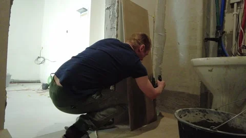 Man cuts tiles for renovation work in a bathroom during daylight hours Stock Footage 332479768