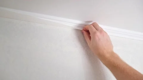 Man cuts wallpaper near ceiling moldings using box cutter and putty blade Stock Footage 201517692