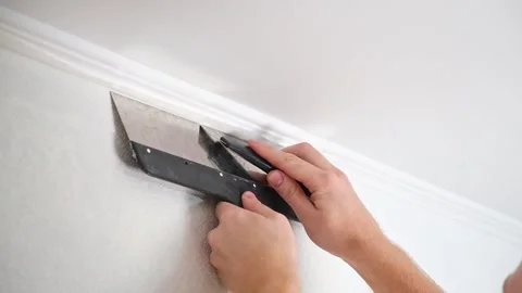 Man cuts wallpaper near ceiling moldings using box cutter and putty blade Stock Footage 201517764