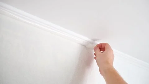 Man cuts wallpaper near ceiling moldings using box cutter and putty blade Stock Footage 203851966