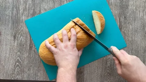 A man cuts white bread on a wooden table on a blue cutting board Video stock 188091738