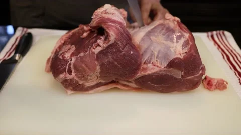 Man Cutting and trimming Large Pork Meat In A Kitchen With Two Knives Video stock 140553334