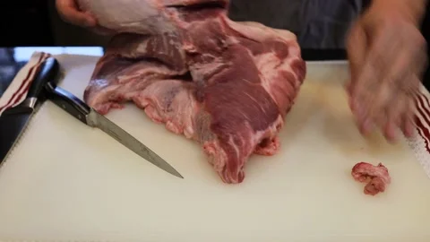 Man Cutting and trimming Large Pork Meat In A Kitchen With Two Knives Stock Footage 140554397