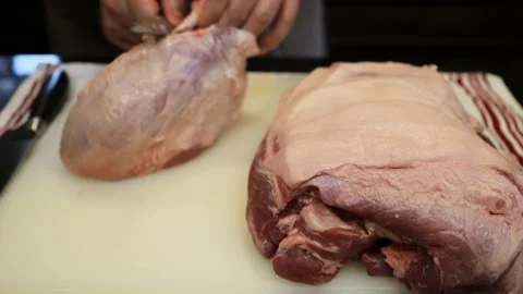 Man Cutting and trimming Large Pork Meat In A Kitchen With Two Knives Stock Footage 140554765