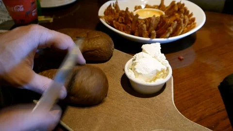 Man cutting black bread with knife at restaurant with butter and blooming onion Stock Footage 90156468