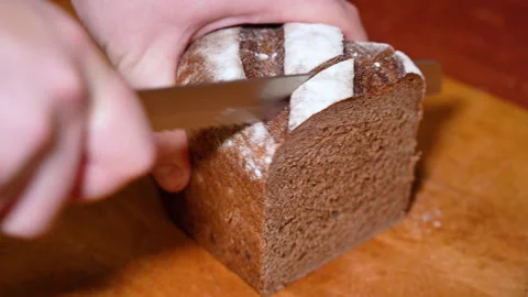Man cutting bread with a kitchen knife on a wooden board Stock Footage 249536989