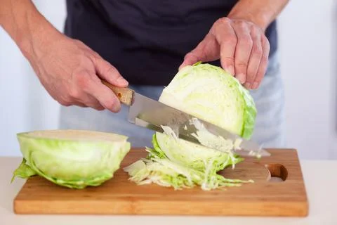 A man cutting a cabbage on a cutting board Stock Photos