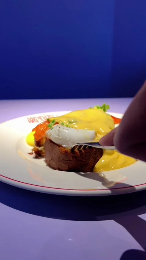 Man cutting eggs benedict with toast and red fish on a plate in a restaurant Stock Footage 274471905