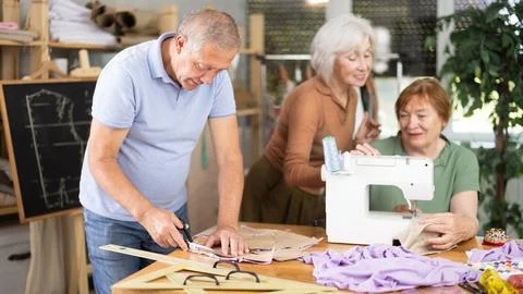 Man cutting fabric along pattern during sewing session for seniors Stock Photos
