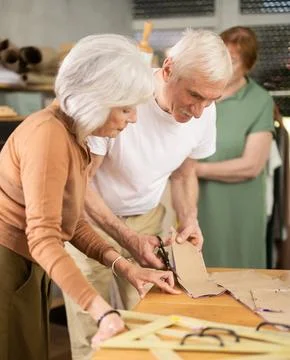 Man cutting fabric along pattern during sewing session for seniors 库存照片