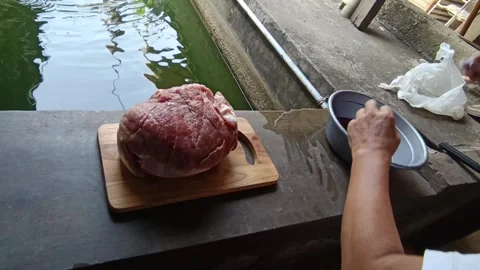 Man Cutting Fresh Beef by the Fish Pond with Green Surroundings in Daylight Stock Footage 283637900