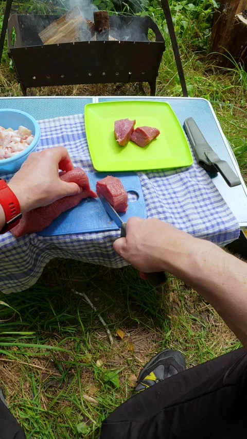 Man cutting fresh raw meat with knife for outdoor picnic barbecue camping l.. 動画素材 344310055