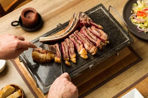 Man cutting a grilled steak with bone on a cooking stone Foto stock
