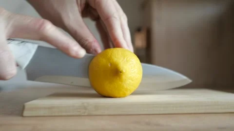 Man cutting a lemon in half with a cooking knife on chopping wooden board close Stock Footage 247205710