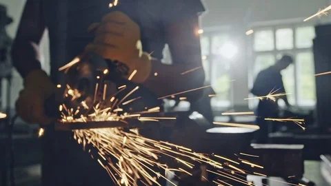 Man cutting metal with angle grinder, working indoors in workshop. Bright sparks Stock Footage 97746882