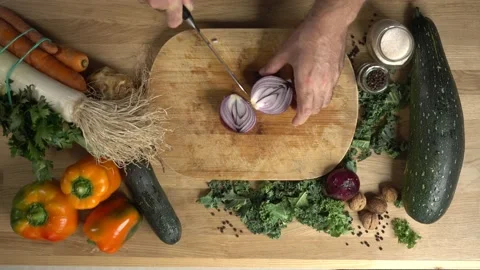 A man is cutting an onion on a table full of fresh vegetables.  Stock Footage 142577752