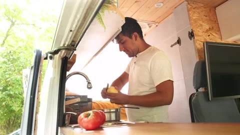 Man cutting potatoes for meal in the kitchen of his camper van. Van road tr.. Video stock 329226190