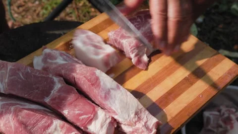 Man cutting raw lamb meat on wooden board outdoors in slomo Stock Footage 319661536