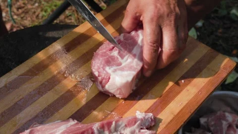 Man cutting raw lamb meat on wooden board outdoors in slomo Stock Footage 319661546