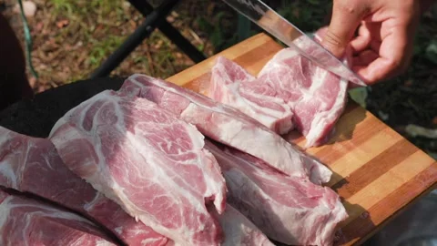 Man cutting raw lamb meat on wooden board outdoors in slomo Stock Footage 319661617