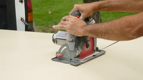 Man Cutting Sheet of Wood on Tailgate of Truck with Skill Saw Stockbeeldmateriaal 104890311