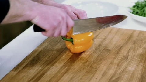 Man cutting sweet peppers with sharp knife on wooden cutting board in kitchen 4K Stock Footage 132287653