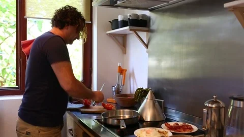 Man Cutting Tomatoes While Preparing Eggs And Bacon Breakfast Video stock 97443896