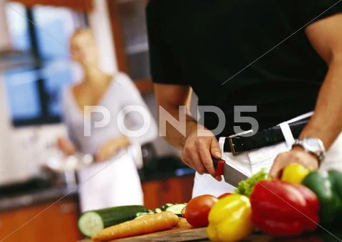 Man Cutting Vegetables, Mid-Section, Woman Standing In Background