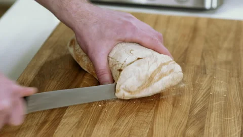Man cutting white bread with sharp knife on wooden cutting board in kitchen. 4K Vídeo Stock 132287348