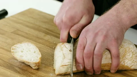 Man cutting white bread with sharp knife on wooden cutting board in kitchen. 4K Stock Footage 132288838
