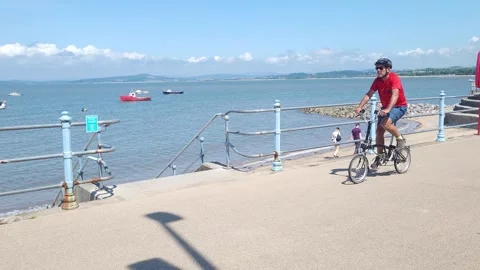 Man cycles past camera on Brompton folding bike, Morecambe UK Stock Footage 244325327