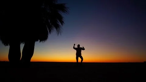 A man dances on the beach against the backdrop of the setting sun. Colorful Stock Footage 82850901