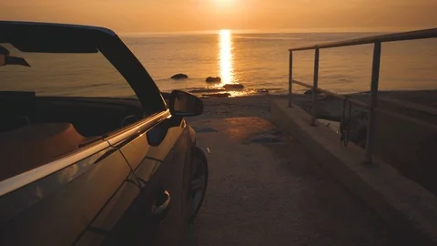 Man dances on driver place in cabriolet car during sunset. Sun sets into the sea Stock Footage 99003102
