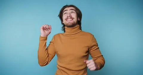 Man dances happily in a studio with a blue background during afternoon hours Vídeo Stock 328249935