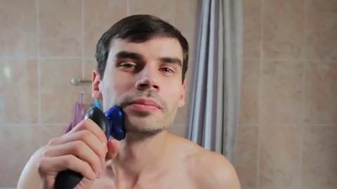 The man dances while shaving. a guy in a good mood shaving with an electric Vídeos de archivo 81691135