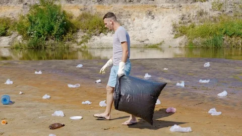 Man dancing and collects plastic trash on banks of polluted river Stock Footage 124313941