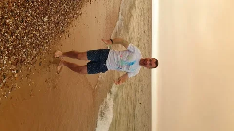 A man is dancing on the beach with a hat. Vertical video Stock Footage 166740164