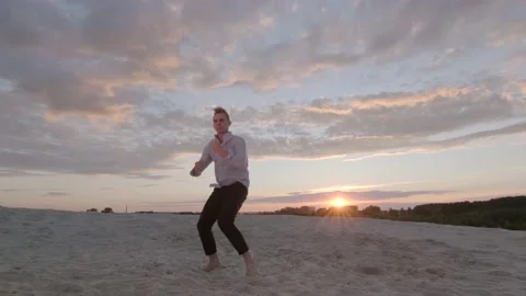 Man dancing freestyle dance on the sand at sunset. Slow motion. Gimbal shot Stock Footage 135610648