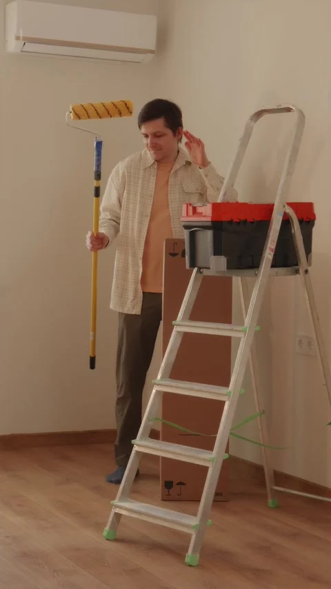 Man dancing with paint roller near toolbox and stepladder Stock Footage 346396322